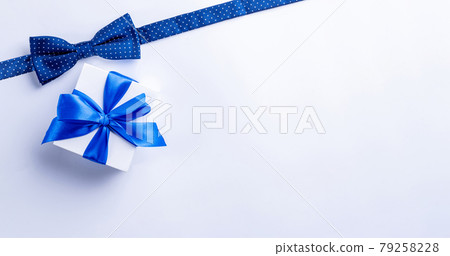 Fathers gift. White box with bow ribbon, blue bowtie or tie on light background. Concept of Fathers Day greeting card, copy space for text. Fathers gift. White box with bow ribbon, blue bowtie or tie on light background. Concept of Fathers Day greeting card, copy space for text. 79258228