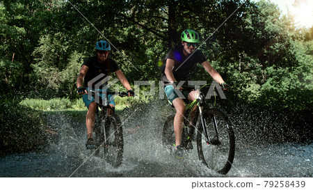 Mountain bikers speeding through forest stream. 79258439