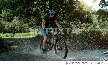 Mountain biker speeding through forest stream. 79258440