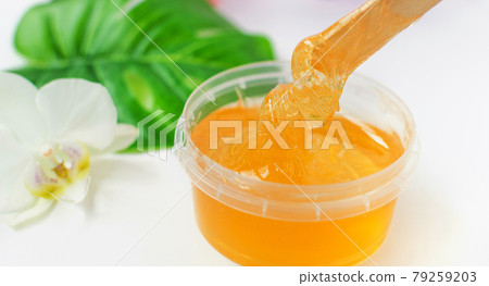 Sugar paste or wax honey in a transparent jar and white orchid on a white background. Sugaring. Depilation and beauty concept. 79259203