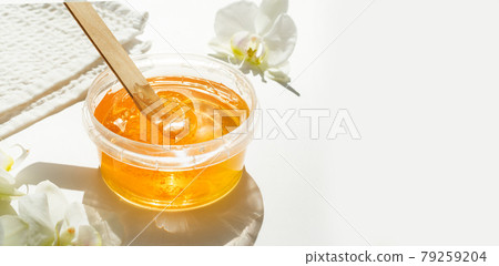 Sugar paste or wax honey in a transparent jar and white orchid on a white background. Sugaring. Depilation and beauty concept. Waxing. 79259204