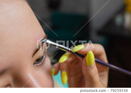 Beautician making depilation with wax strip young woman's eyebrows in spa center. Attractive woman getting facial care at beauty salon. 79259336