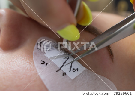 Beautiful Woman with long eyelashes in a beauty salon. Eyelash extension procedure. Lashes close up. Beautiful Woman with long eyelashes in a beauty salon. Eyelash extension procedure. Lashes close up. 79259601