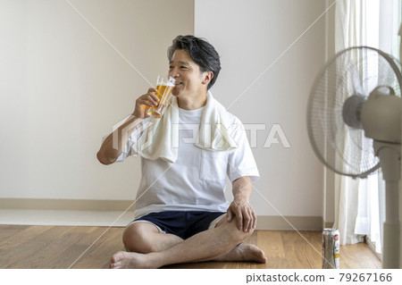 Image of a man in his 50s drinking beer in front of an electric fan after taking a bath Image of a man in his 50s drinking beer in front of an electric fan after taking a bath 79267166