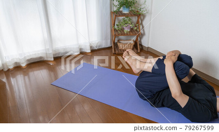 一個人在房間裡做瑜伽。胎兒姿勢（Pindersana）。伸展下半身和臀大肌。 79267599