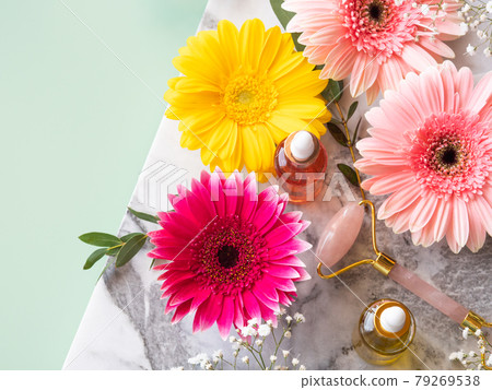 Pink quartz face roller gua sha and serum in bottle on marble table. Skin care concept with flowers 79269538