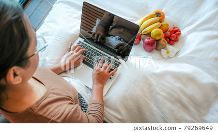Picture of tourists hand used laptop and eating fruits on the bed in the luxury hotel room, healthy food concept Picture of tourists hand used laptop and eating fruits on the bed in the luxury hotel room, healthy food concept 79269649