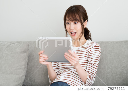 A woman surprised while looking at a tablet device 79272211