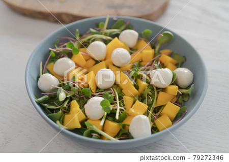 Salad with mango, mozzarella and mixed microgreens in blue bowl on white oak table Salad with mango, mozzarella and mixed microgreens in blue bowl on white oak table 79272346