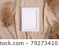 Picture frame with blank paper card mockup near to pampas dry grass on beige neutral colored textile 79273410