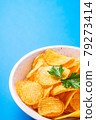 Fried corrugated golden potato chips with parsley leaf in wooden bowl on blue background, angle view macro 79273414
