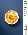 Fried corrugated golden potato chips with parsley leaf in wooden bowl on blue background, top view 79273415