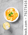 Fresh ice cold water drink with lemon near to fried corrugated golden potato chips with parsley leaf in wooden bowl on concrete background, top view 79273416