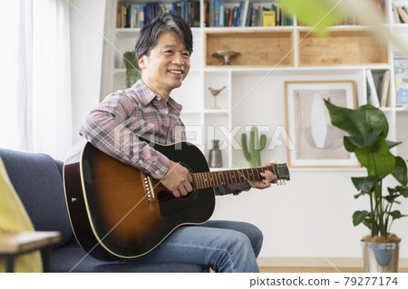 A smiling man in his 50s with an acoustic guitar 79277174