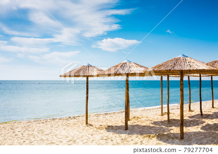 Row of wooden umbrellas at sandy beach, sea and blue sky Row of wooden umbrellas at sandy beach, sea and blue sky 79277704