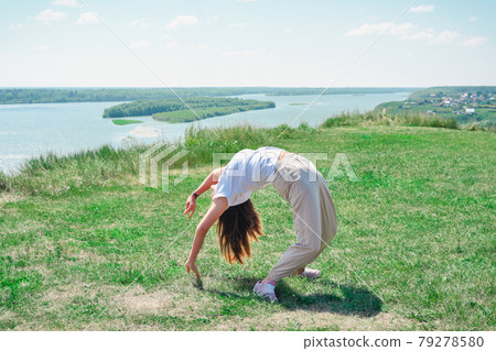 slim beautiful woman doing yoga and stretching outdoors. young woman exercising alone on a river bank. person enjoying summer active lifestyle 79278580