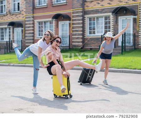 Three joyful Caucasian friends are having fun and chasing each other while riding a suitcase. Excited women go on a road trip. The brunette blonde and the redhead are going on vacation. Three joyful Caucasian friends are having fun and chasing each other while riding a suitcase. Excited women go on a road trip. The brunette blonde and the redhead are going on vacation. 79282908