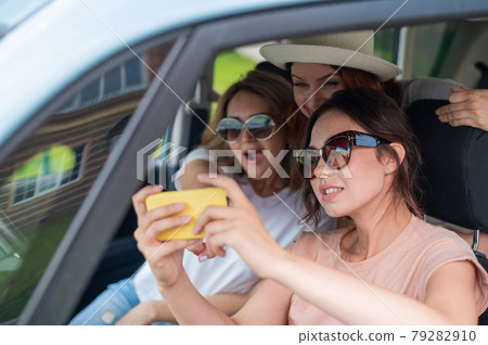 Three girlfriends go on a road trip and take a selfie on a smartphone. The woman is sitting in the car and taking pictures with her mobile. Vacation travel. Three girlfriends go on a road trip and take a selfie on a smartphone. The woman is sitting in the car and taking pictures with her mobile. Vacation travel. 79282910