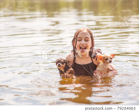 The child enjoys relationships with dogs. A girl with two chihuahuas swims in the river. The child enjoys relationships with dogs. A girl with two chihuahuas swims in the river. 79284063