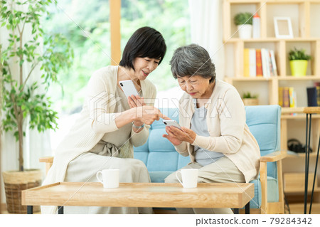 Parents and children who talk with each other while looking at their smartphones, mother-in-law, mother and child, senior women, and two middle-aged women 79284342