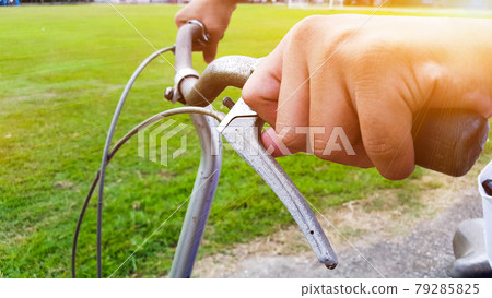 Hands are on a vintage bike handle which the break shaft tip is broken, the handle is at closed to the green field Hands are on a vintage bike handle which the break shaft tip is broken, the handle is at closed to the green field 79285825