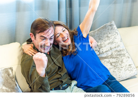 Mature couple celebrating something they are watching on TV. Mature couple celebrating something they are watching on TV. 79289856