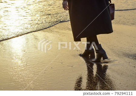 A woman in heels walking along the beach 79294111