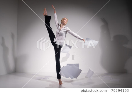 A graceful ballerina in a business suit throws documents in the studio. Business woman dance barefoot on a white background A graceful ballerina in a business suit throws documents in the studio. Business woman dance barefoot on a white background 79294193