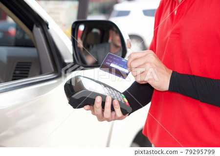 Gas station staff swipe mockup credit card via payment terminal after giving a price quote to the customer sitting in the car. Gas station staff swipe mockup credit card via payment terminal after giving a price quote to the customer sitting in the car. 79295799