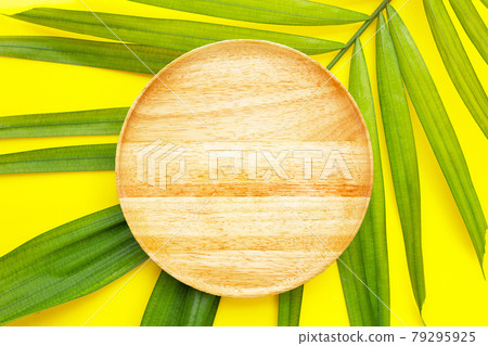 Empty wooden plate on tropical palm leaves on yellow background. Empty wooden plate on tropical palm leaves on yellow background. 79295925