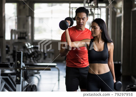 trainer set biceps dumbbell position to girl in gym 79297958