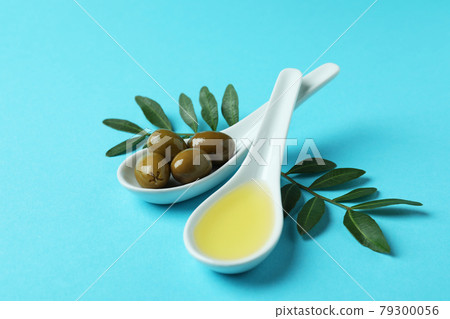 Spoons with olives and oil, and twigs on blue background Spoons with olives and oil, and twigs on blue background 79300056