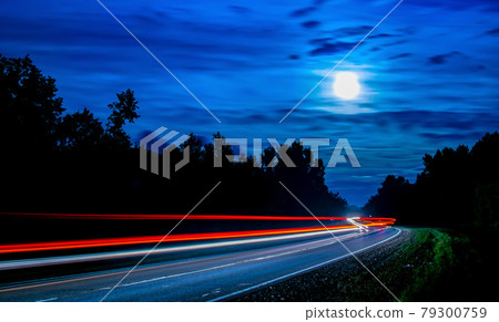long lines of light from cars passing along the night forest long lines of light from cars passing along the night forest 79300759