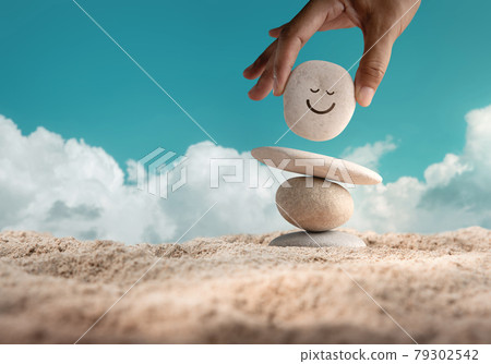 Enjoying Life Concept. Harmony and Positive Mind. Hand Setting Natural Pebble Stone with Smiling Face Cartoon to Balance on Beach Sand. Balancing Body, Mind, Soul and Spirit. Mental Health Practice Enjoying Life Concept. Harmony and Positive Mind. Hand Setting Natural Pebble Stone with Smiling Face Cartoon to Balance on Beach Sand. Balancing Body, Mind, Soul and Spirit. Mental Health Practice 79302542