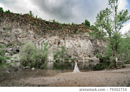 The bride in a white wedding dress on the bank of a mountain river. The bride in a white wedding dress on the bank of a mountain river. 79302710