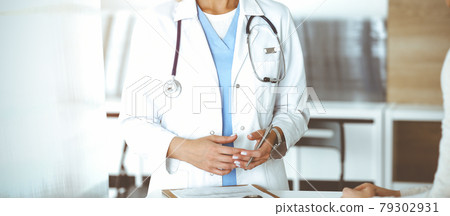 Unknown woman-doctor communicating with female patient in sunny clinic. Physician checks medical history record and exam results, close-up Unknown woman-doctor communicating with female patient in sunny clinic. Physician checks medical history record and exam results, close-up 79302931