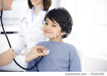 Doctor-woman examining a child patient by stethoscope. Cute arab boy at physician appointment. Medicine concept Doctor-woman examining a child patient by stethoscope. Cute arab boy at physician appointment. Medicine concept 79302993