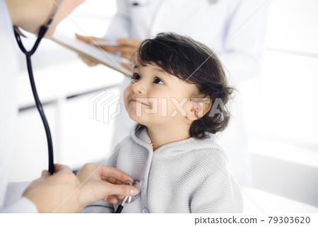 Woman-doctor examining a child patient by stethoscope. Cute arab toddler at physician appointment. Medicine concept Woman-doctor examining a child patient by stethoscope. Cute arab toddler at physician appointment. Medicine concept 79303620