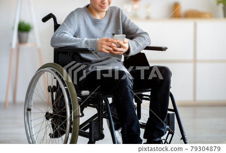 Unrecognizable disabled teen boy in wheelchair using cellphone, browsing web or posting in social media at home Unrecognizable disabled teen boy in wheelchair using cellphone, browsing web or posting in social media at home 79304879