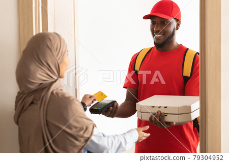 Smiling deliveryman holding POS machine, woman paying with card Smiling deliveryman holding POS machine, woman paying with card 79304952