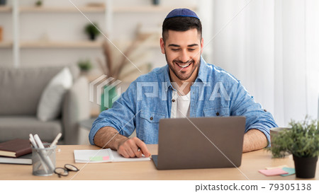 Smiling israeli man working on laptop at home Smiling israeli man working on laptop at home 79305138