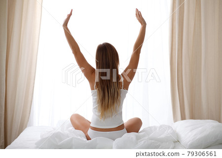 Woman stretching in bed after wake up, back view, entering a day happy and relaxed after good night sleep. Sweet dreams, good morning, new day, weekend, holidays concept 79306561