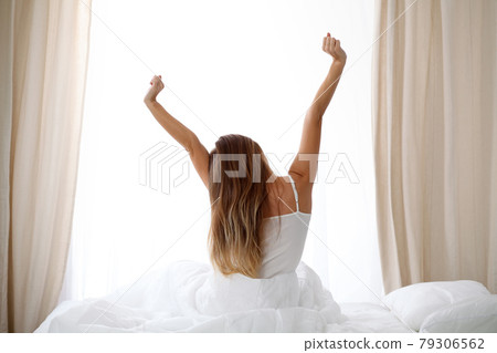 Woman stretching in bed after wake up, back view, entering a day happy and relaxed after good night sleep. Sweet dreams, good morning, new day, weekend, holidays concept 79306562