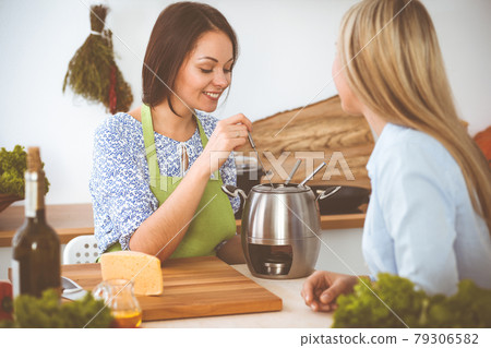 Two women friends taste new recipes for delicious fondue while sitting at the kitchen table. Healthy meal cooking concept 79306582