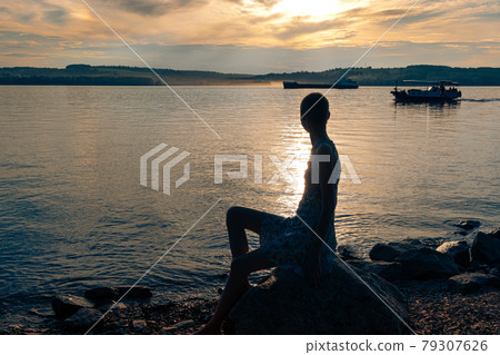 teen girl sitting on the banks of the river, looking at the ships 79307626
