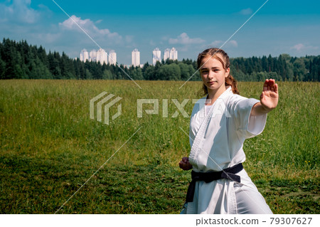 teen girl training karate kata outdoors, performing a strike oi zuki 79307627