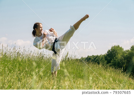 teen girl training karate kata outdoors, performs the mawashi geri kick 79307685