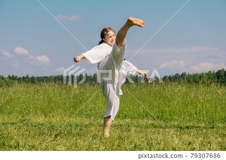 teen girl training karate kata outdoors, performs roundhouse kick ushiro mawashi geri 79307686