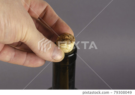 Wine bottle with broken cork and hand on gray background. 79308049