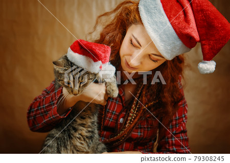 Woman in Santa Claus hat with cat in Christmas hat. 79308245